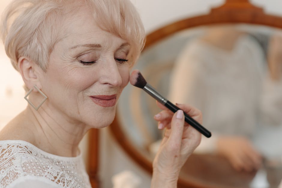 Close-up of a senior woman applying makeup while smiling gracefully indoors.