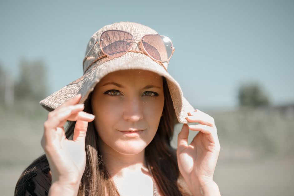 A woman wearing a stylish hat with sunglasses, enjoying a bright summer day outdoors.