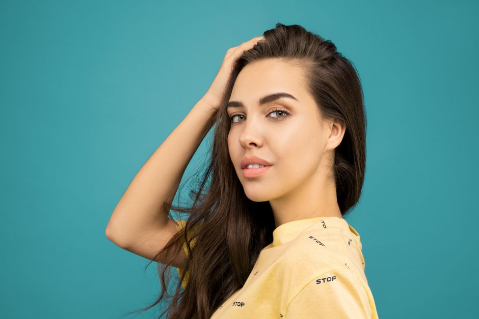 Elegant portrait of a woman in a yellow top posing against a teal background.