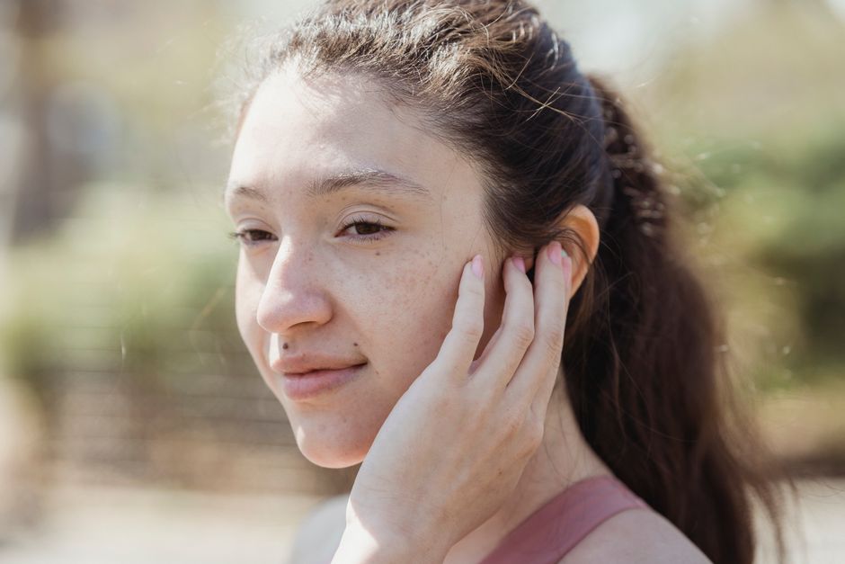 Close-up portrait of a woman gently touching her face while outdoors. Capturing natural beauty.