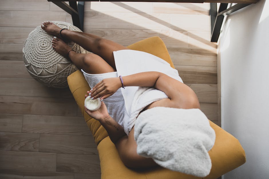 A woman sits in a comfortable chair applying skincare in natural light.
