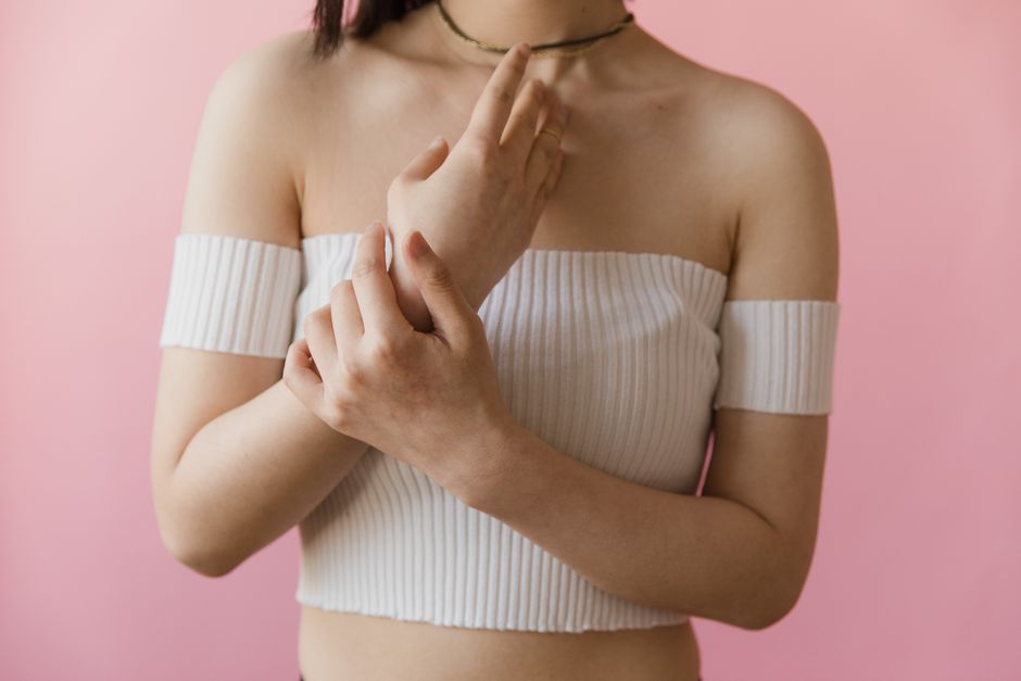 Close-up portrait of a woman posing in a white off-the-shoulder top against a pink background.