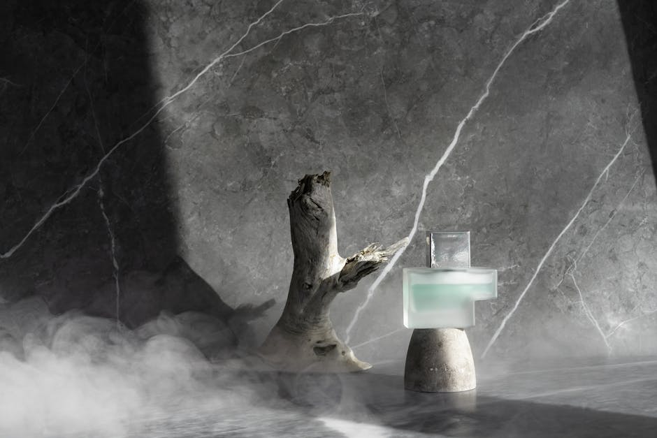 Stylish perfume bottle on marble with driftwood and smoke in modern artistic setup.