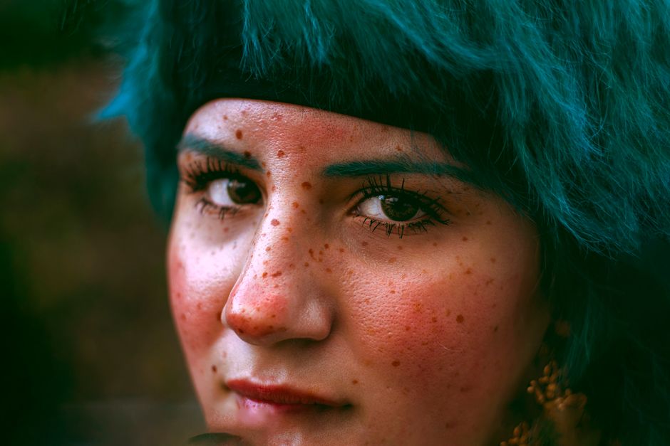 Close-up portrait of a woman with freckles and striking blue hair.