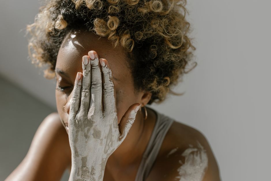 A serene portrait of a woman with clay-covered skin and curly hair, evoking beauty and creativity.