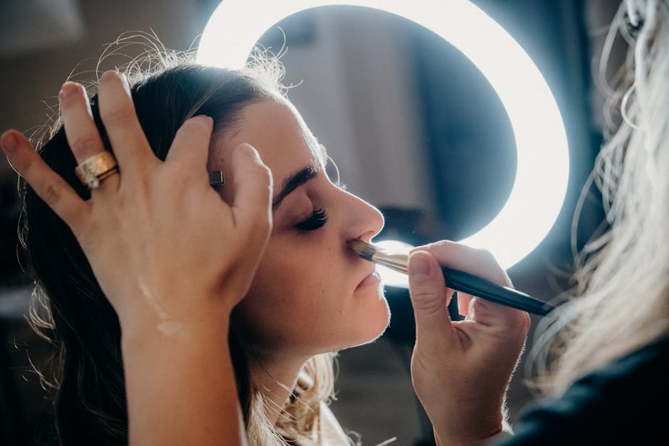 Close-up of a woman receiving makeup under a ring light by a professional artist.