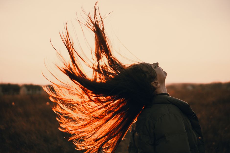 Dynamic shot of a woman flipping her hair in an outdoor sunset scene.