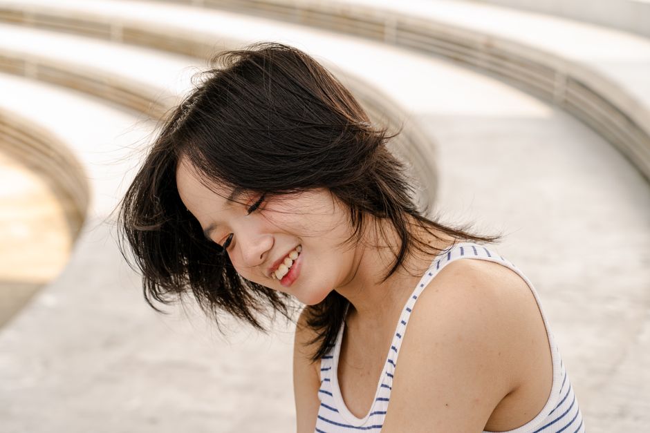 Young woman smiling in outdoor setting with a striped top, enjoying a sunny day.