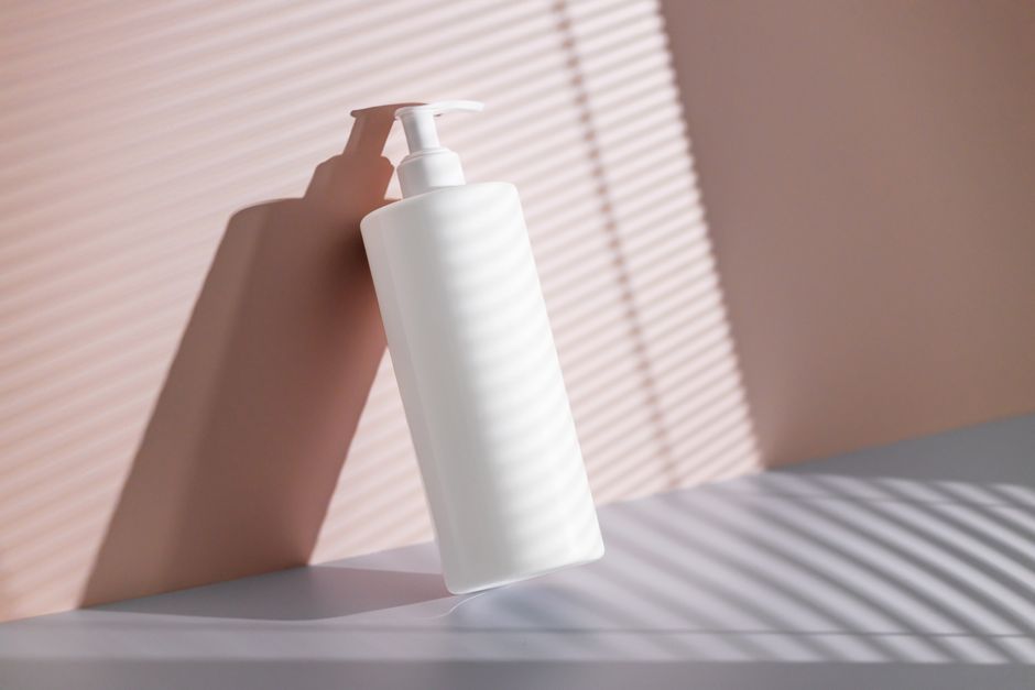 White pump bottle casting shadow in sunlight with pink background, ideal for cosmetic branding.