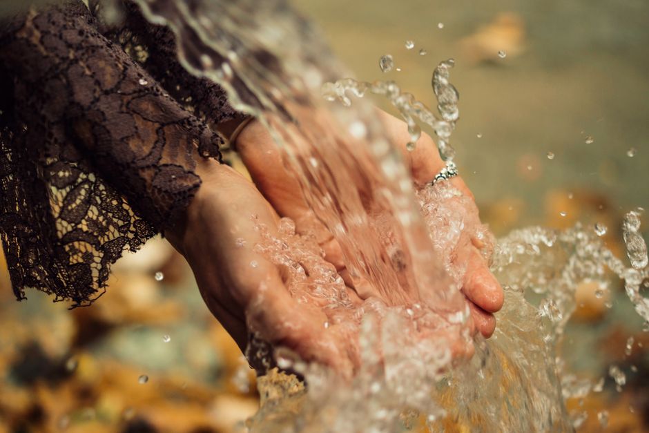 Hands catching flowing water outdoors, symbolizing freshness and purity.