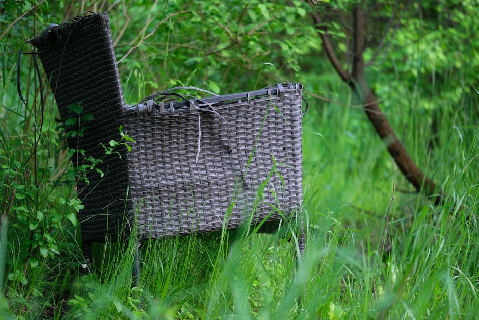 An abandoned wicker chair surrounded by vibrant grass and foliage, creating a serene and rustic outdoor scene.
