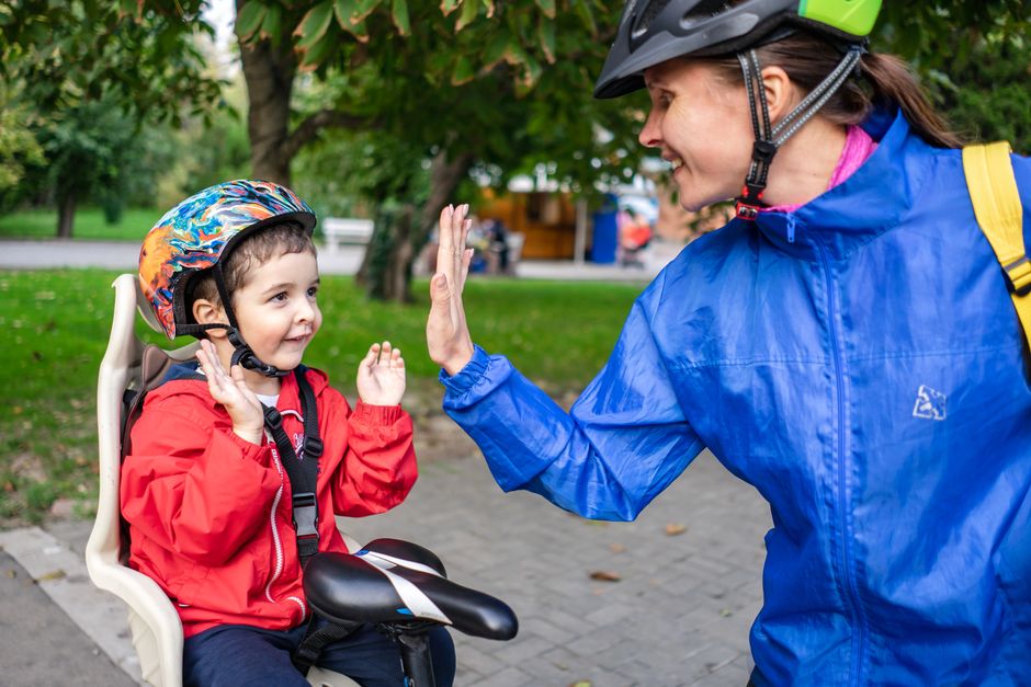 A joyful mother and child high-fiving during a bicycle ride in the park, capturing a moment of happiness and bonding.