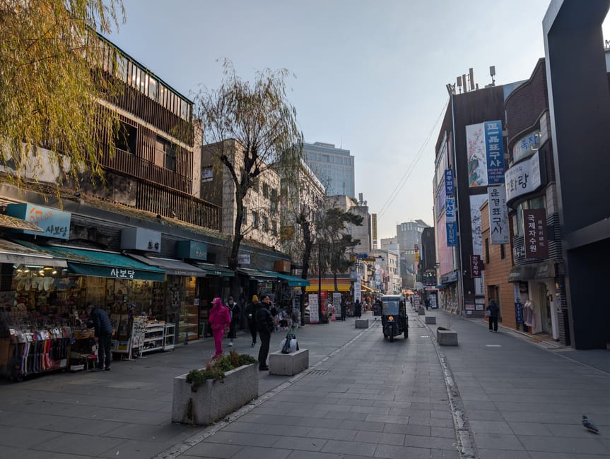 Vibrant street in Seoul with shops and a few people walking. Captured on a clear day, showcasing local architecture.