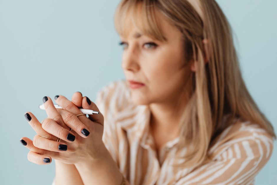 Blurred image of a woman holding a pen with a thoughtful expression, focusing on her hands.