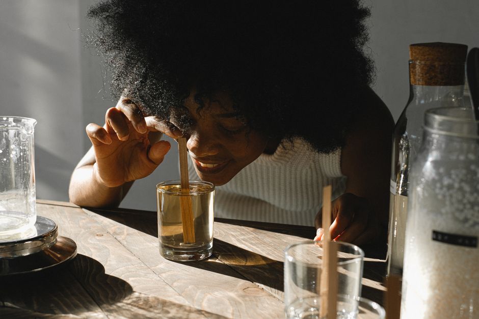 A woman explores a glass of liquid in a sunlit room, engaging with its scent.