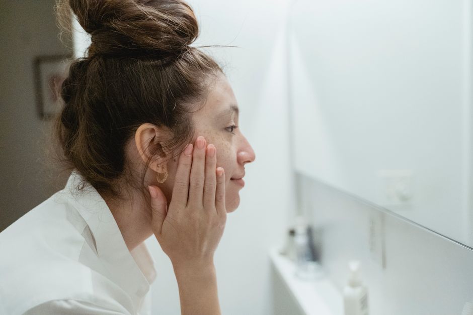 Profile view of a woman touching her face and reflecting in the bathroom mirror.