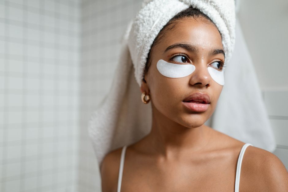 A young woman with a towel on her head applying under eye masks as part of her skincare routine.