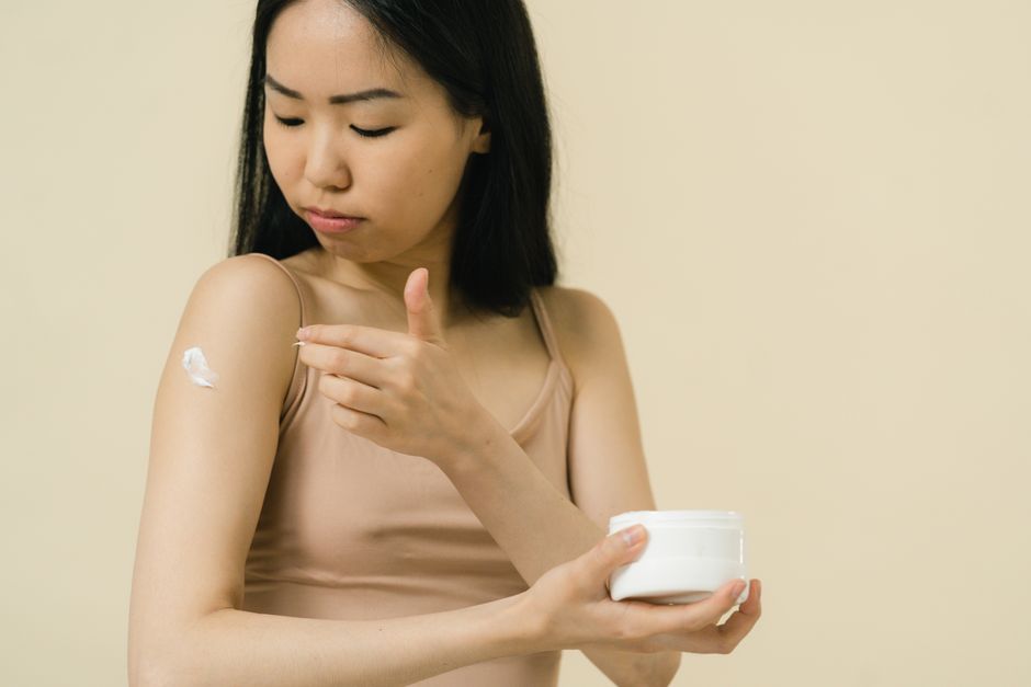 A woman applies moisturizing cream on her arm, focusing on skincare and self-care.