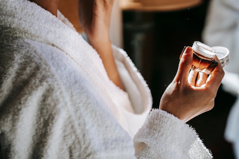 Side view of crop anonymous ethnic female with jar of moisturizing cream against mirror during daily routine