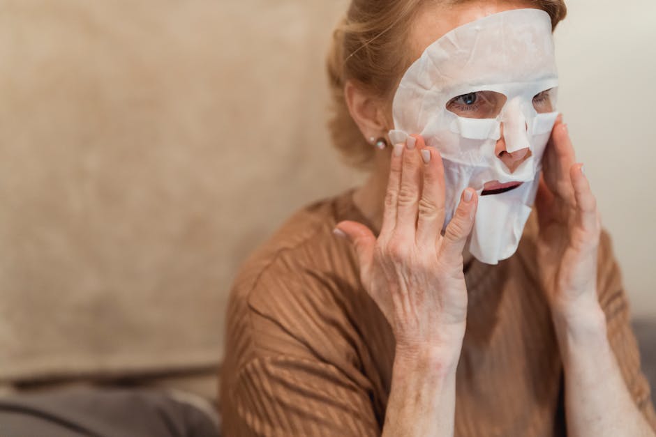 A senior woman applies a hydrating sheet mask for skincare indoors, focusing on facial rejuvenation.