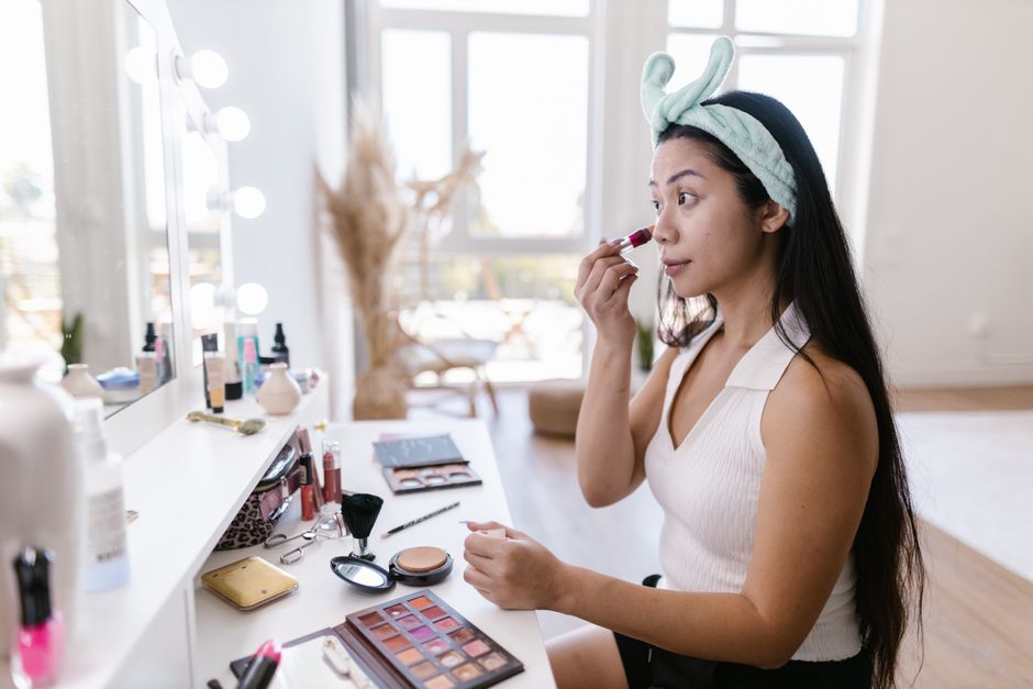 A woman in a headband applying makeup in a bright room with a vanity mirror.