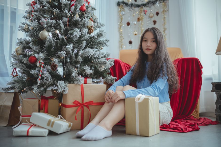 Young woman sitting by a decorated Christmas tree with presents. Cozy holiday setting indoors.