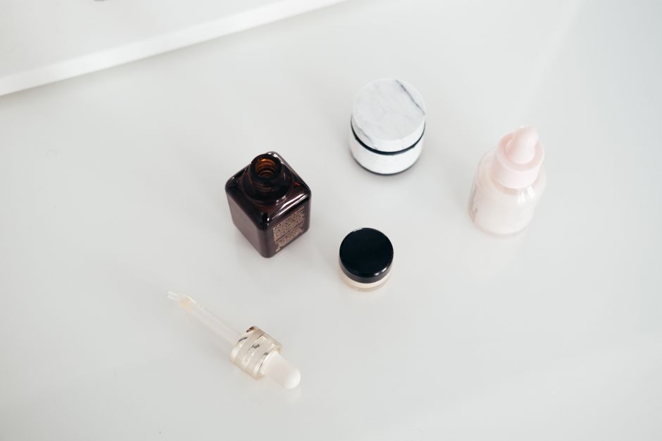 From above of open flacon of aroma oil near pipette and beauty products on smooth white surface